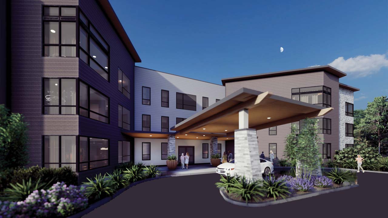 A modern three-story building with large windows and a covered entrance driveway, where people stand near a white car. Landscaping with green plants and purple flowers lines the front. The sky is clear with a crescent moon visible.