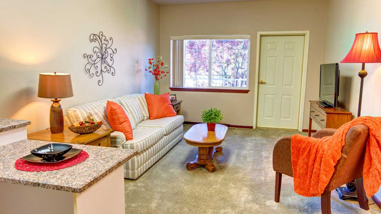 Bright living room with striped sofa, orange accents, wooden coffee table, TV, lamps, wall art, and large window letting in natural light. Cozy and inviting decor.